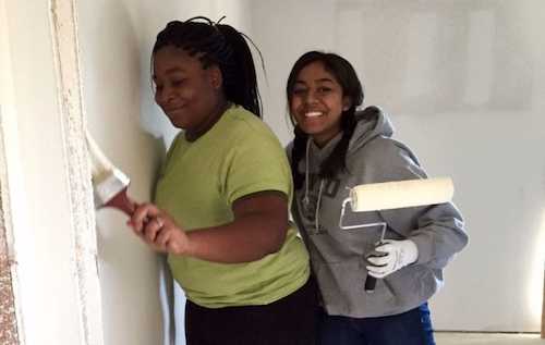 Volunteers painting a wall with paint rollers